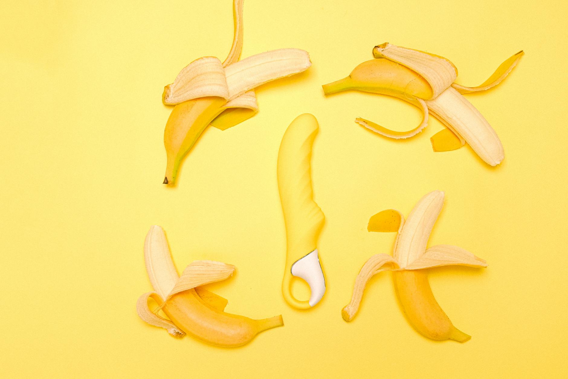 Yellow lemon-shaped vibrator on yellow background with fresh lemons