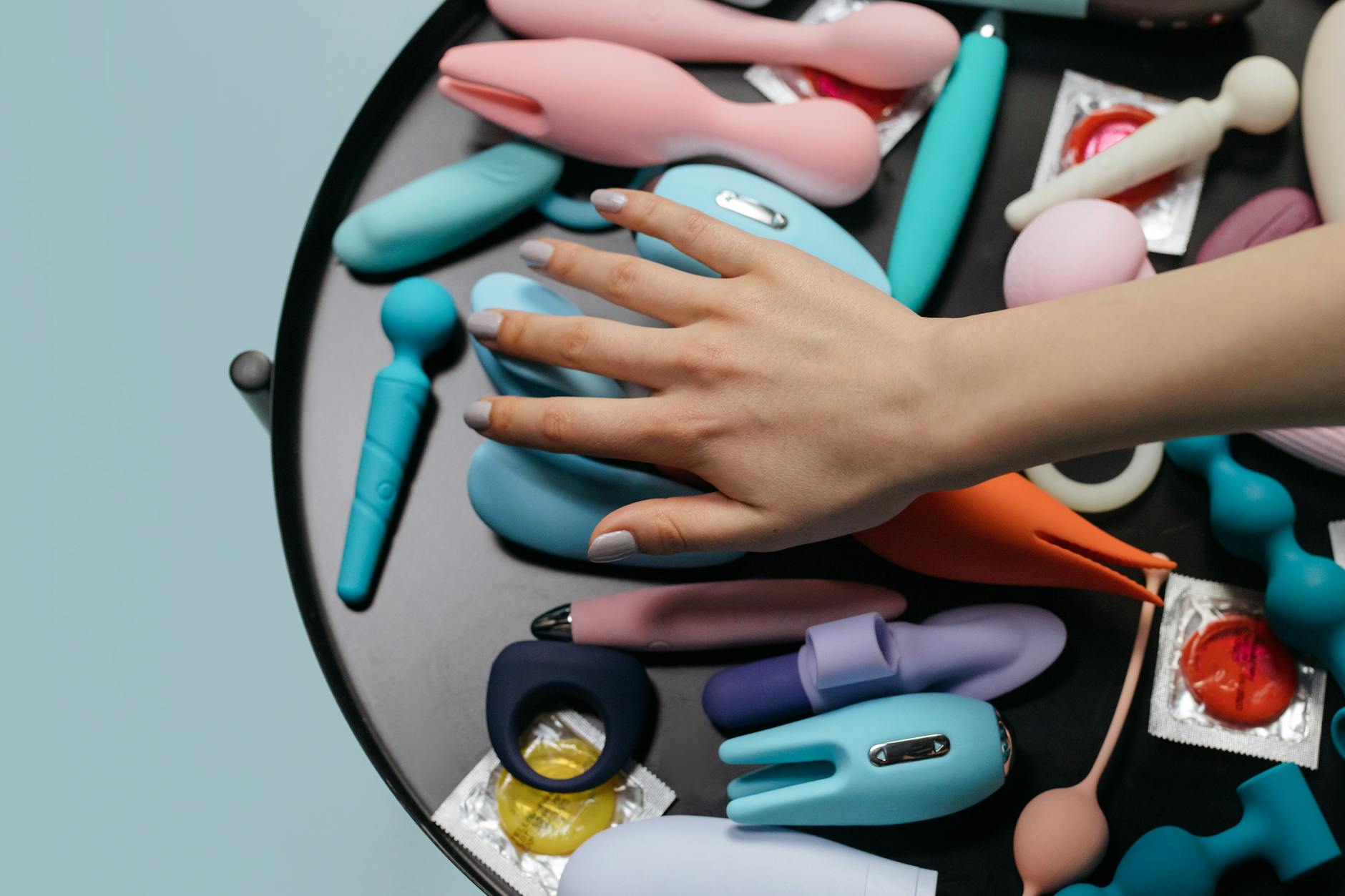 Hand reaching over a variety of colorful sex toys arranged on a table