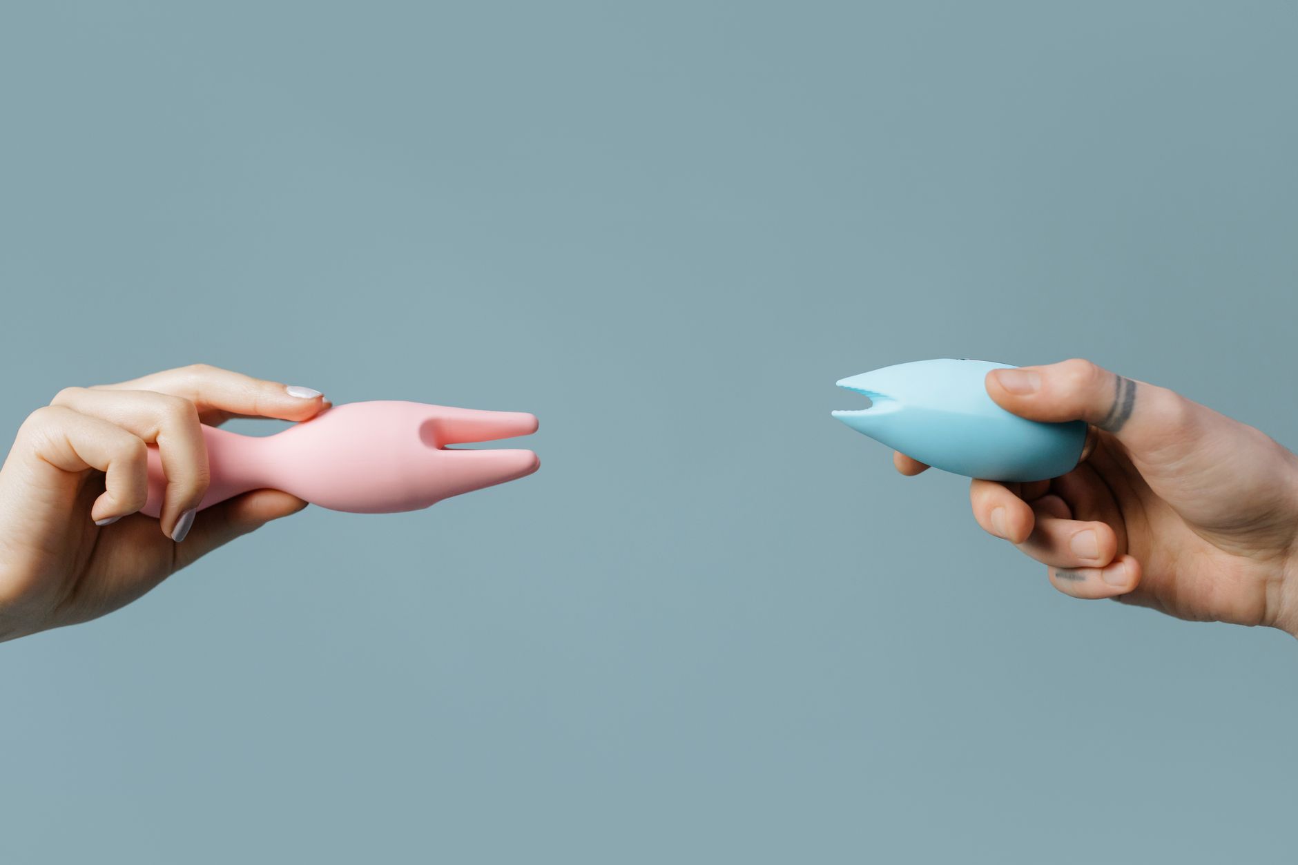 Person holding blue and pink silicone vibrators in a thoughtful, contemplative moment